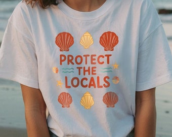 May include: A white t-shirt with a graphic design featuring seashells and the text "Protect the Locals".