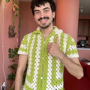 May include: A green and white crocheted short-sleeved shirt with a button-up front.