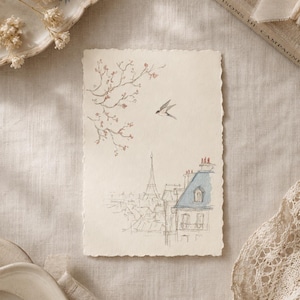 May include: A rectangular off-white paper card with deckled edges featuring a delicate ink and watercolor illustration of a Parisian cityscape with the Eiffel Tower, a flying bird, and a flowering branch with small pink blossoms.