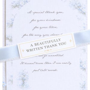 Puede incluir: Una tarjeta de agradecimiento con una cinta azul claro. La tarjeta tiene un diseño floral y el texto "A BEAUTIFULLY WRITTEN THANK YOU". El mensaje incluye frases como "gracias especiales" y "por tu amabilidad".
