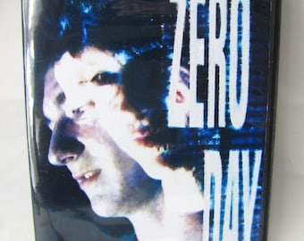 May include: A DVD case featuring a dark, high-contrast profile portrait of a person with dark hair. The text ZERO DAY is printed in large, white, distressed capital letters on the right side against a blue and black digital background.
