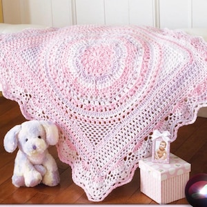 Puede incluir: Una manta de bebé de ganchillo rosa y blanca, con un borde festoneado. La manta está sobre una superficie blanca. Un perro de peluche y una pequeña foto enmarcada sugieren un tema de guardería.
