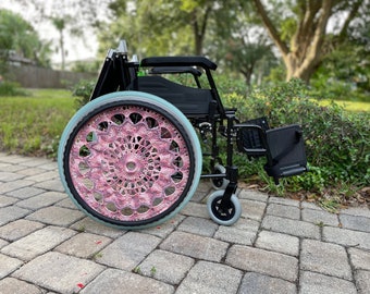 May include: A black wheelchair with a pink and white crocheted wheel cover. The wheelchair is on a brick walkway.