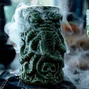 May include: A green ceramic mug shaped like a monster with tentacles and a skull. The mug is filled with smoke.