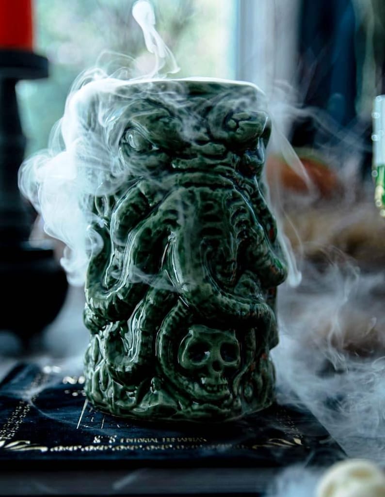 May include: A green ceramic mug shaped like a monster with tentacles and a skull. The mug is filled with smoke.