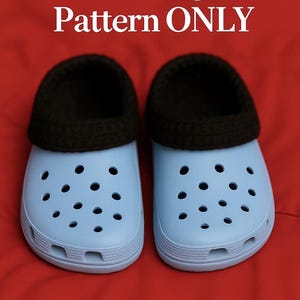 Könnte beinhalten: Zwei hellblaue Clogs mit schwarzen Häkeleinsätzen, vor rotem Hintergrund. Die Clogs haben mehrere runde Löcher. Der Text oben lautet "Crochet Clog Insert Pattern ONLY". Das The Crafty Cult-Logo befindet sich unten.