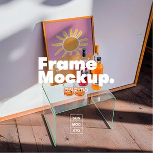 May include: A clear glass table with a framed artwork featuring a yellow sun on a pink background. Several bottles of liquor and two glasses are on the table. The text "Frame Mockup" is displayed in white.