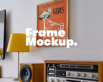 May include: A framed vintage poster with the text "CLYDE FITCH'S GREATEST COMEDY GIRLS" hangs on a white wall. A yellow lamp and wooden stereo equipment sit below. The image also contains the text "Frame Mockup."
