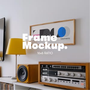 Op de afbeelding: Een interieur met een ingelijste geometrische print, een gele lamp en een houten stereosysteem. Het frame heeft een lichte houten afwerking. De tekst "Frame Mockup. 16x6 RATIO" wordt in het wit weergegeven.