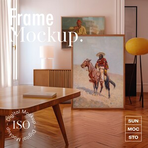 Puede incluir: Una obra de arte enmarcada que representa a una persona a caballo en un paisaje desértico. La obra está colgada en una pared blanca en una habitación con una mesa de madera y una lámpara. El texto "Frame Mockup" es visible en la esquina superior izquierda de la imagen.