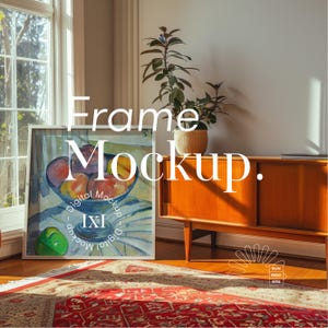 May include: A white picture frame with a painting of fruit in a bowl. The frame is sitting on a wooden floor in front of a wooden cabinet. The cabinet has a light wood finish and a single door. The frame is in a room with a window and a plant in a pot.