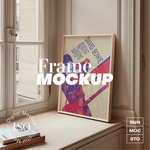 Pode incluir: Um pôster emoldurado com um design vintage que apresenta um músico tocando guitarra. O pôster é intitulado "David Bowie" e inclui o texto "RollArena Leeds 29th June 1973". O pôster está encostado em um peitoril de janela com uma pilha de livros abaixo.