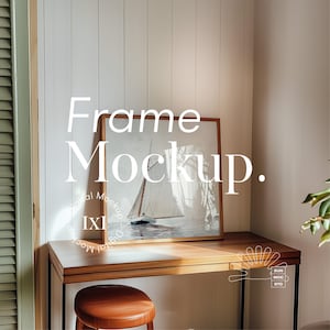 May include: A wooden frame mockup with a painting of a sailboat on the water. The frame is on a wooden desk with a stool in front of it. The wall behind the desk is white with vertical wood paneling.