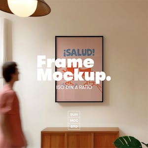 Könnte beinhalten: Ein gerahmtes Poster mit dem Text "¡SALUD!" in Blau und Orange und den Worten "Frame Mockup" in Weiß. Das Poster befindet sich in einem schwarzen Rahmen und hängt an einer weißen Wand. Das Bild enthält auch einen Holzschrank und eine Person.