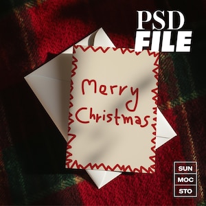 May include: A cream Christmas card with red text saying "Merry Christmas" and a red zig-zag border, inside a white envelope. The card rests on a red and green plaid blanket. The words "PSD FILE" are in the upper right corner of the image.