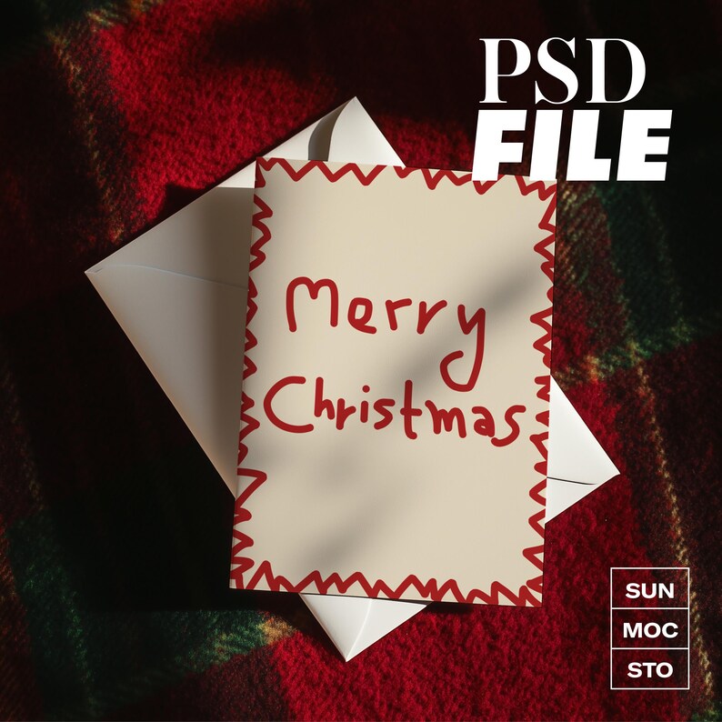 May include: A cream Christmas card with red text saying "Merry Christmas" and a red zig-zag border, inside a white envelope. The card rests on a red and green plaid blanket. The words "PSD FILE" are in the upper right corner of the image.