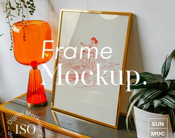May include: A gold picture frame mockup with a white mat and a vintage illustration of a woman in a swimsuit on a surfboard. The frame is sitting on a table with a lamp and a potted plant.