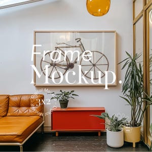 May include: A framed print of a vintage bicycle with the text "Frame Mockup" in white letters. The frame is on a white wall with a red cabinet and plants in pots.