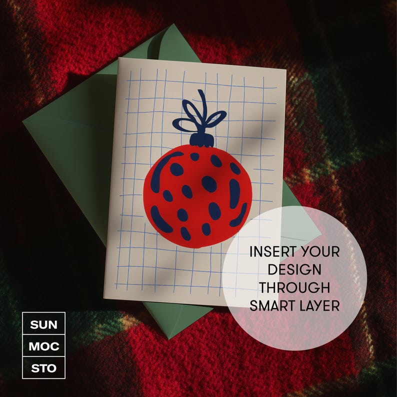 May include: A Christmas card featuring a red and blue bauble design on a grid. The card rests on a green envelope, set against a red and green plaid backdrop. The card includes the text "INSERT YOUR DESIGN THROUGH SMART LAYER".