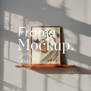 May include: A brown wooden shelf with a framed print of a Japanese style painting of a tree with a red fruit. The print is in a gold frame and the shelf is against a white wall with shadows from a window.