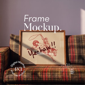 May include: A wooden frame containing a print of a cowboy riding a bucking horse with a lasso and the text Yee haw!! The frame is positioned on a plaid sofa. Text overlay reads Frame Mockup and Digital Mockup 4x3 with a sun logo.