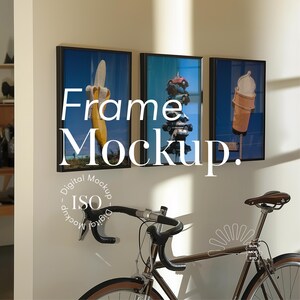 May include: Three framed pictures hanging on a white wall. The pictures are of a banana, a stack of toy cars, and a container of ice cream. A bicycle is in the foreground.