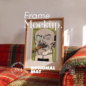 May include: A light wood frame containing a print of a bald man with a monocle and a cigar against a light green background. The text "IMPORT" is visible at the top of the print. The frame is positioned on a red and green plaid surface.
