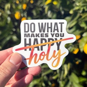 May include: A white sticker with the text "Do what makes you happy" with the word "holy" crossed out. The sticker has a gradient of orange, yellow, and red.