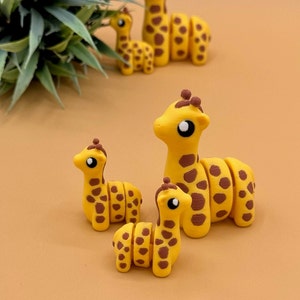 May include: A set of four yellow and brown giraffe figurines. The giraffes are made of a smooth, textured material and have large, black eyes. The giraffes are arranged in a group, with the largest giraffe at the back and the smallest giraffe at the front.
