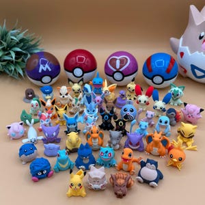 May include: A collection of colourful miniature figurines of various characters, including Pikachu, and several Poké Balls. The figurines are in various poses and colours, set against a neutral background. The toys are likely made of plastic.