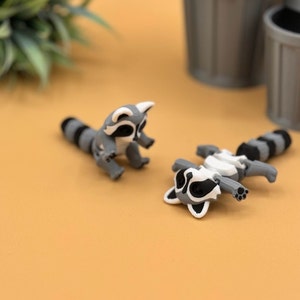 3D printed baby raccoons lay and sit down.
