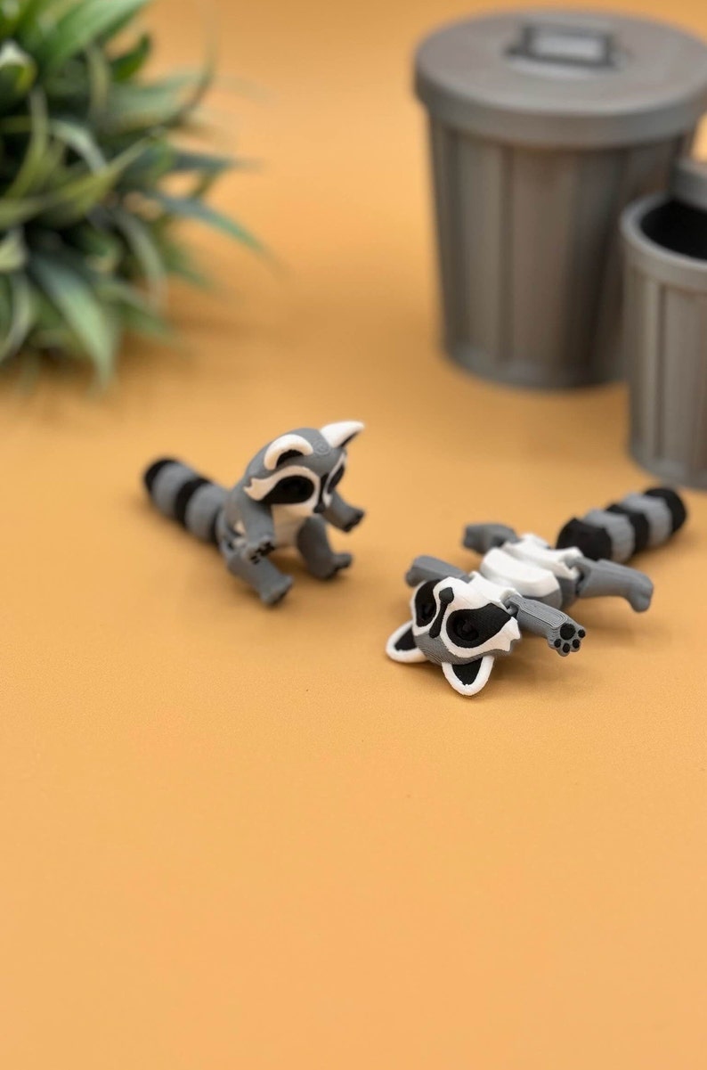 3D printed baby raccoons lay and sit down.