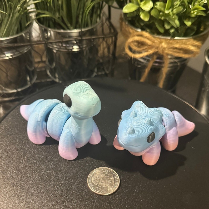 3D printed rainbow dinosaurs at about three inches long by two inches all. This is how the toys compare to a quarter.