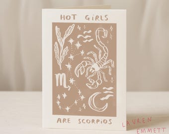 May include: A folded greeting card with a beige background and white illustrations. The card features the text "HOT GIRLS ARE SCORPIOS" and a scorpion, stars, and other celestial designs. The artist's name is also visible.