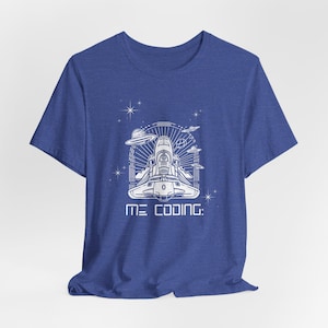 Könnte beinhalten: Ein blaues T-Shirt mit einer weißen Grafik eines Raumschiffs im Weltraum mit dem Text "ME CODING:" darunter.
