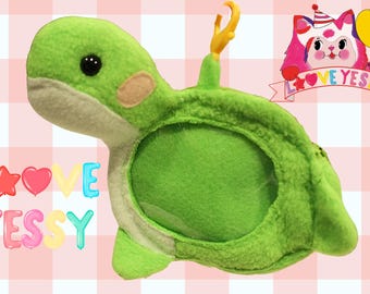 May include: Green plush turtle with a large photo frame opening in the back. The turtle has a smiling face and a small pink nose. The frame is surrounded by a white border.