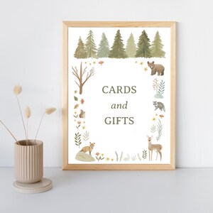 May include: A framed print with a woodland theme, featuring a forest of trees at the top and various animals around the border. The text "CARDS and GIFTS" is centered. The frame is light brown.