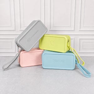 Puede incluir: Cuatro estuches rectangulares en colores pastel: gris, amarillo, rosa y azul. El estuche gris tiene impreso "G-Tube Station". El estuche amarillo tiene una pieza de rompecabezas. El rosa tiene "Sophia" y el azul "THEODORE".