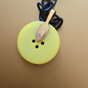May include: A yellow button pendant necklace with a black chain. The button has three holes and a gold-colored clasp.