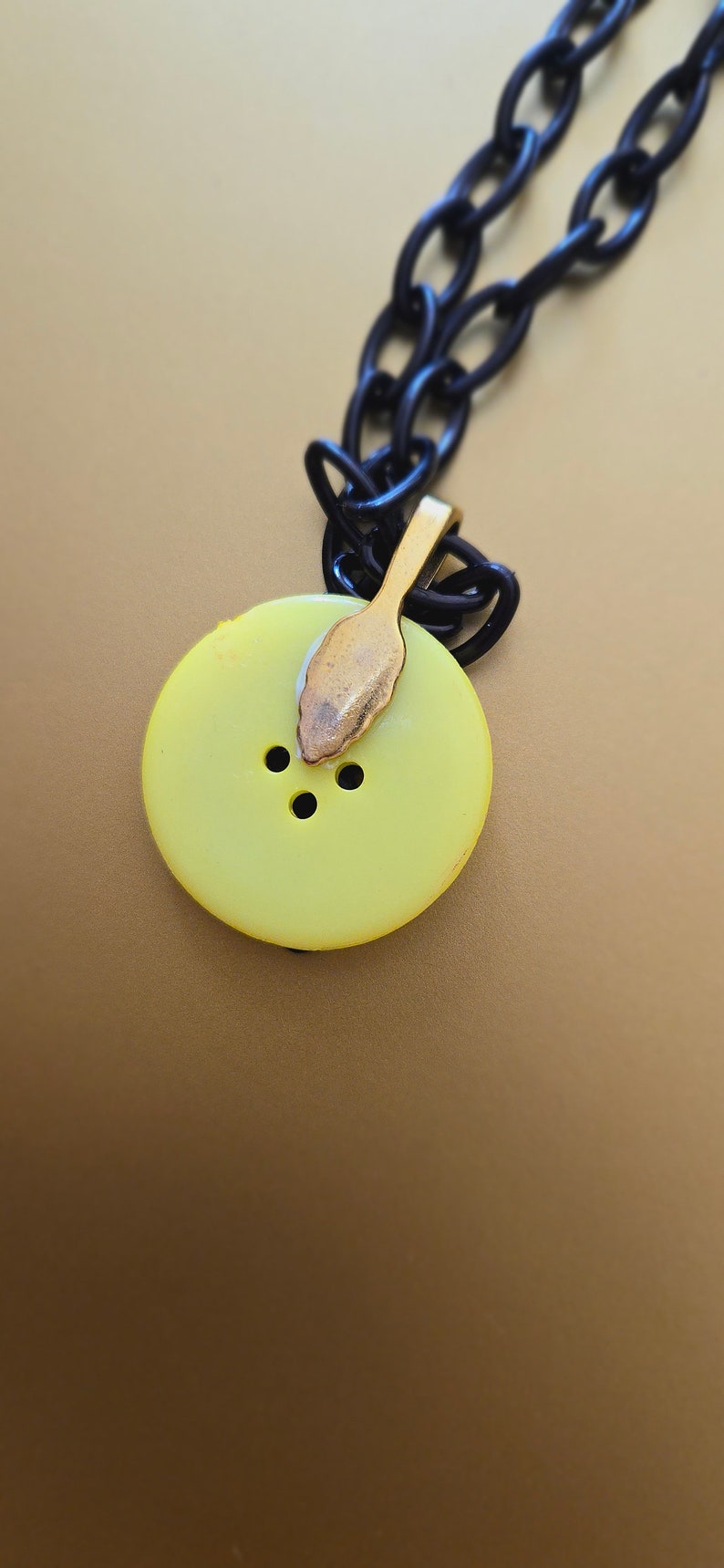 May include: A yellow button pendant necklace with a black chain. The button has three holes and a gold-colored clasp.