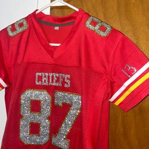 May include: Red football jersey with the number 87 in rhinestones. The jersey has the word "CHIEFS" on the front and the number 8 on each shoulder.