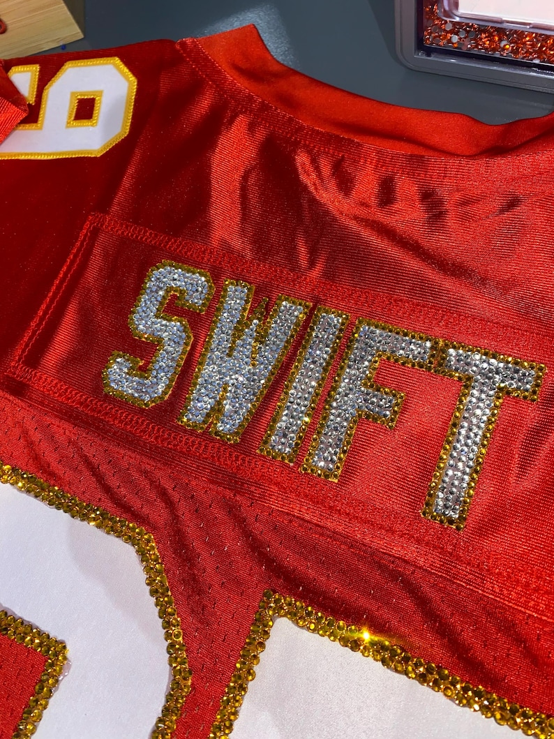 May include: Red football jersey with the number "10" on the shoulder and the word "SWIFT" spelled out in rhinestones on the back.