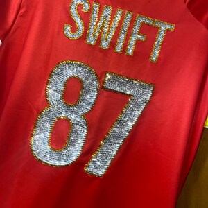 May include: Red jersey with the name "SWIFT" and the number "87" in rhinestones.