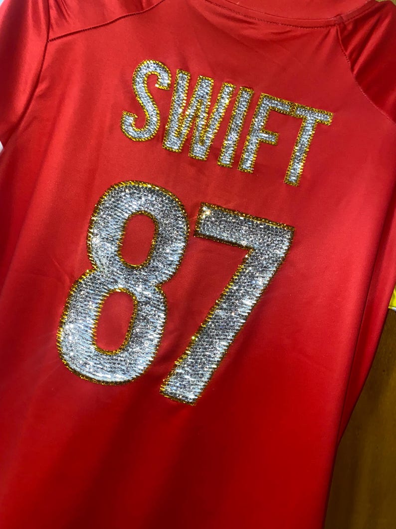 May include: Red jersey with the name "SWIFT" and the number "87" in rhinestones.