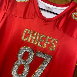 May include: Red football jersey with the word "CHIEFS" and the number "87" in gold and rhinestones.