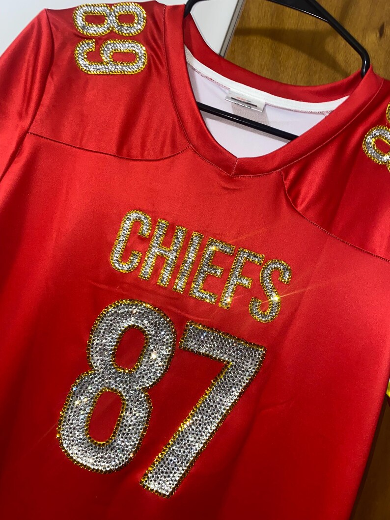 May include: Red football jersey with the word "CHIEFS" and the number "87" in gold and rhinestones.