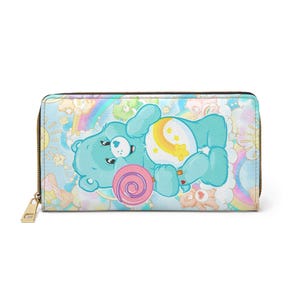 Pode incluir: Uma carteira azul clara com zíper, com um urso de desenho animado com um pirulito. O urso está deitado em um fundo de arco-íris, nuvens e estrelas. A carteira tem um zíper dourado e um puxador correspondente.