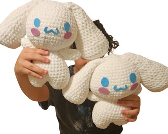 Op de afbeelding: Twee witte gehaakte knuffels met blauwe en roze gezichtskenmerken. De knuffels houden elkaars hand vast en hebben een lieve uitdrukking.