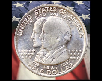 May include: A silver-colored 1921 Alabama Centennial half dollar coin featuring the profiles of William Wyatt Bibb and Thomas Kilby. The text reads UNITED STATES OF AMERICA, IN GOD WE TRUST, BIBB, KILBY, 1921, and HALF DOLLAR, with stars.