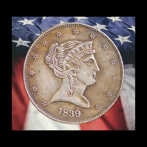 Pu&ograve; includere: Una moneta d'argento con la scritta "LIBERTY" sopra il profilo di una donna. La moneta &egrave; datata 1839 e circondata da stelle. Lo sfondo presenta la bandiera americana. Il diametro &egrave; di circa 3,8 cm.